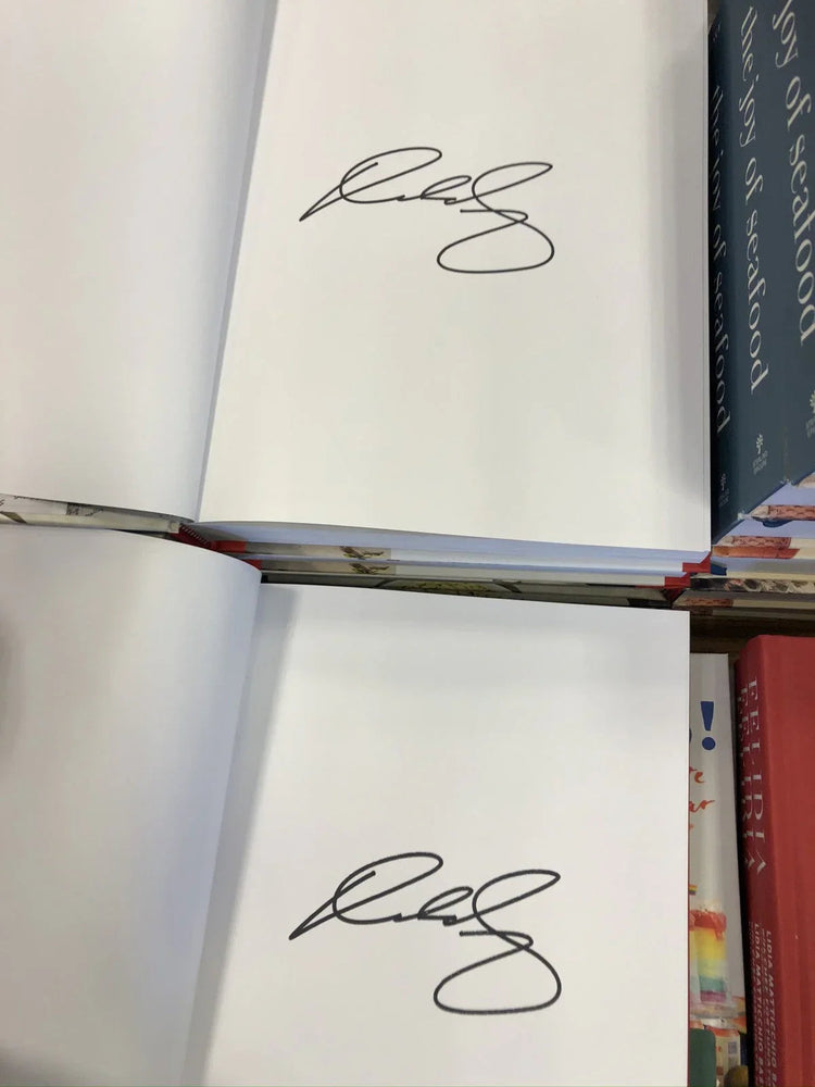 Two open books with identical signatures on blank pages, surrounded by other hardcover books.