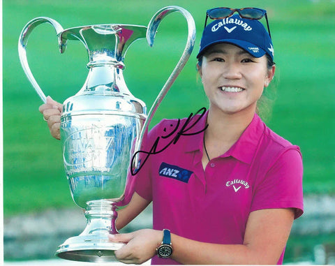 Smiling female golfer holding large trophy, wearing Callaway cap and pink shirt, with autograph