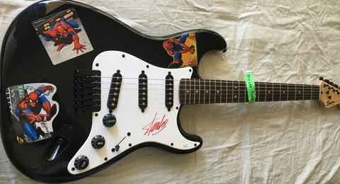Black electric guitar with Spider-Man stickers and a prominent signature on the pickguard