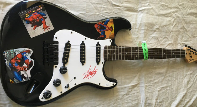 Black electric guitar with Spider-Man stickers and a prominent signature on the pickguard