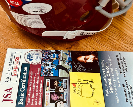 Maroon NCAA football helmet with certification sticker and James Spence Authentication card on wooden surface