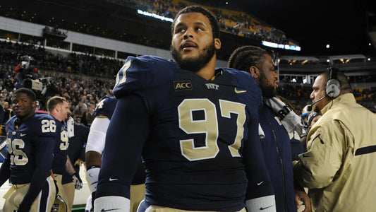American football player in navy blue Pitt uniform number 97 on the sidelines of a stadium at night