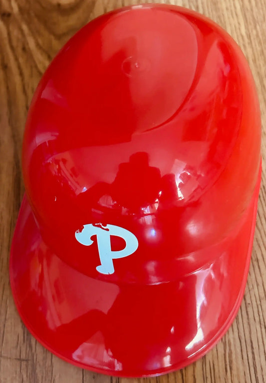 Red plastic baseball helmet with white P logo on wooden surface, Philadelphia Phillies memorabilia