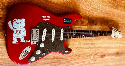 Red Ted movie guitar with signed autograph, featuring Ted bear graphic and 'F#%! You, Thunder!' text on wood floor