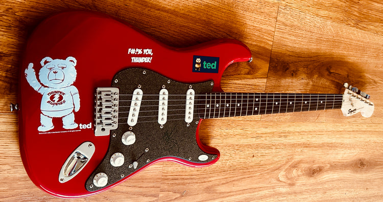 Red Ted movie guitar with signed autograph, featuring Ted bear graphic and 'F#%! You, Thunder!' text on wood floor
