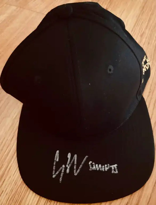 Black baseball cap autographed and inscribed with 'Squints' on bill, on wood floor